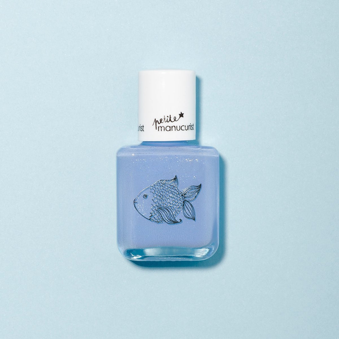 Un flacon de vernis à ongles bleu clair non toxique pour enfants Pomme the Fish de Manucurist, orné d’une illustration de poisson et d’un bouchon blanc, sur fond bleu pâle.