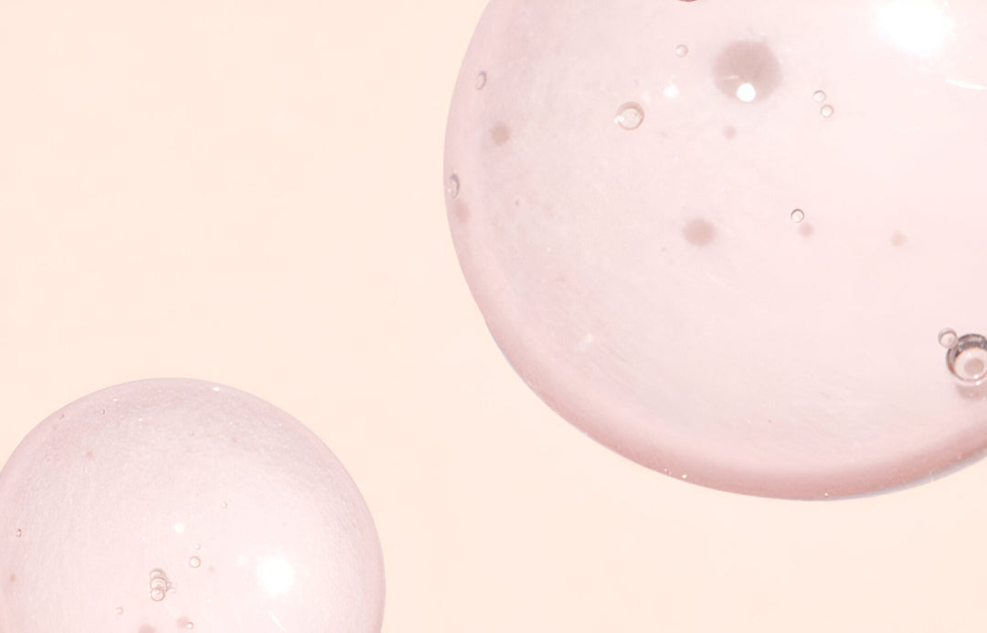 Two large, translucent pink bubbles with tiny air bubbles inside float against a pale pink background. The bubbles overlap slightly in the images lower left and upper right corners.