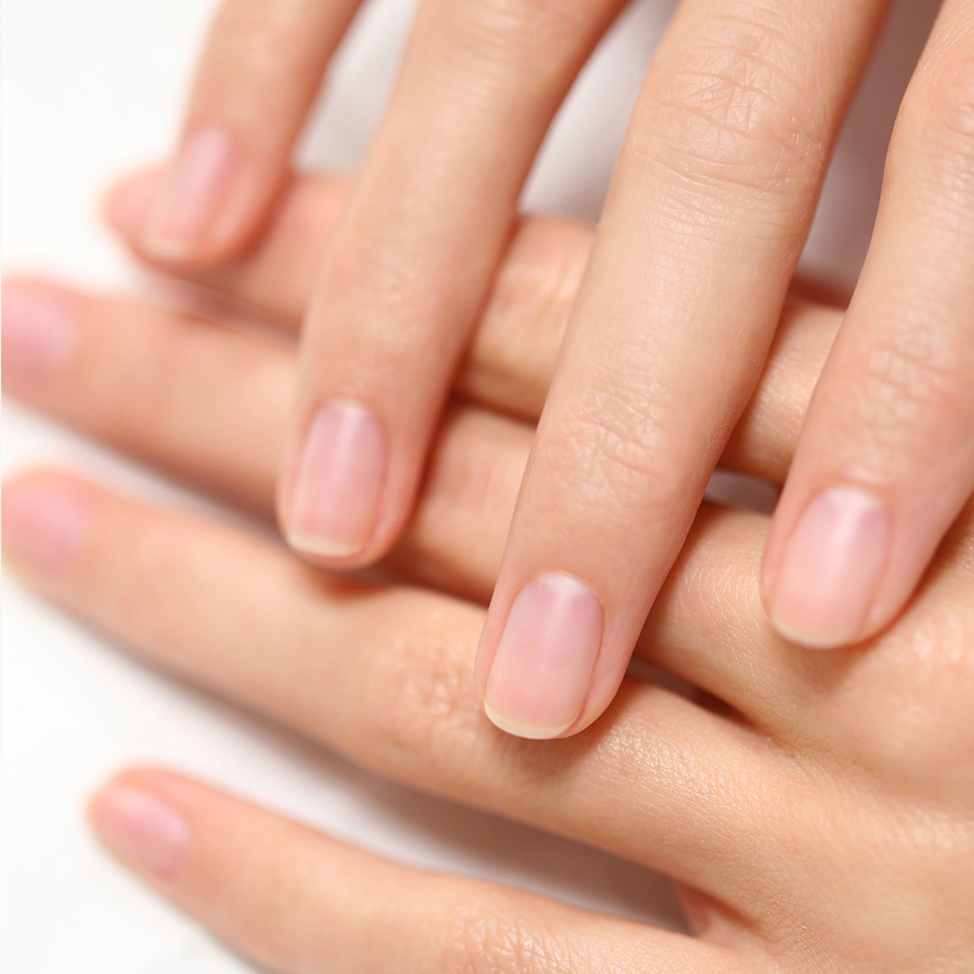 Close-up of well-groomed hands with natural, clean fingernails resting on a light surface. The nails are short and healthy, with no polish or decorations.