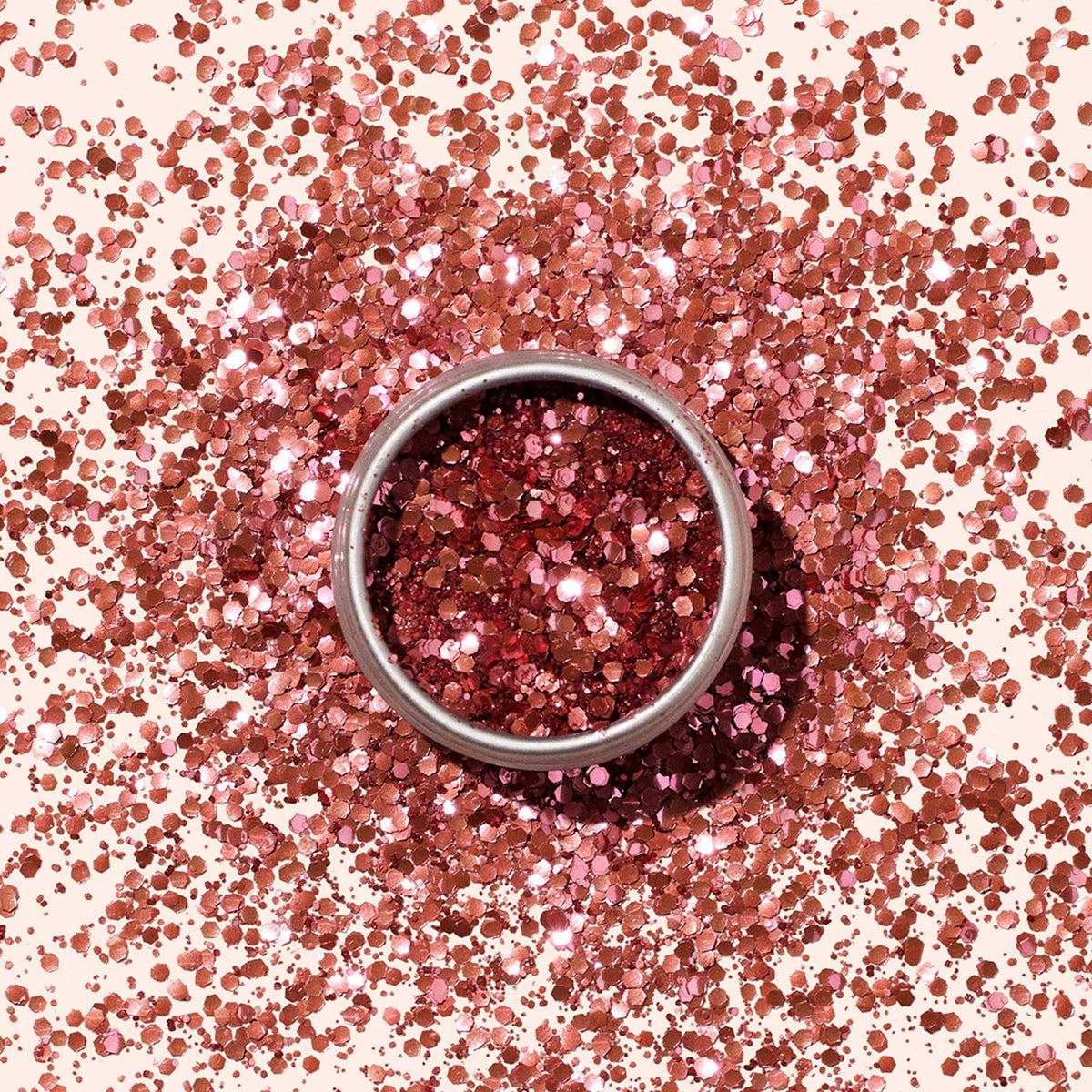 Les Paillettes biodégradables de Manucurist, présentées dans un contenant rond en métal, brillent dans des nuances de rose — idéales pour le Nail Art — tandis que des paillettes roses sont dispersées sur une surface beige clair.