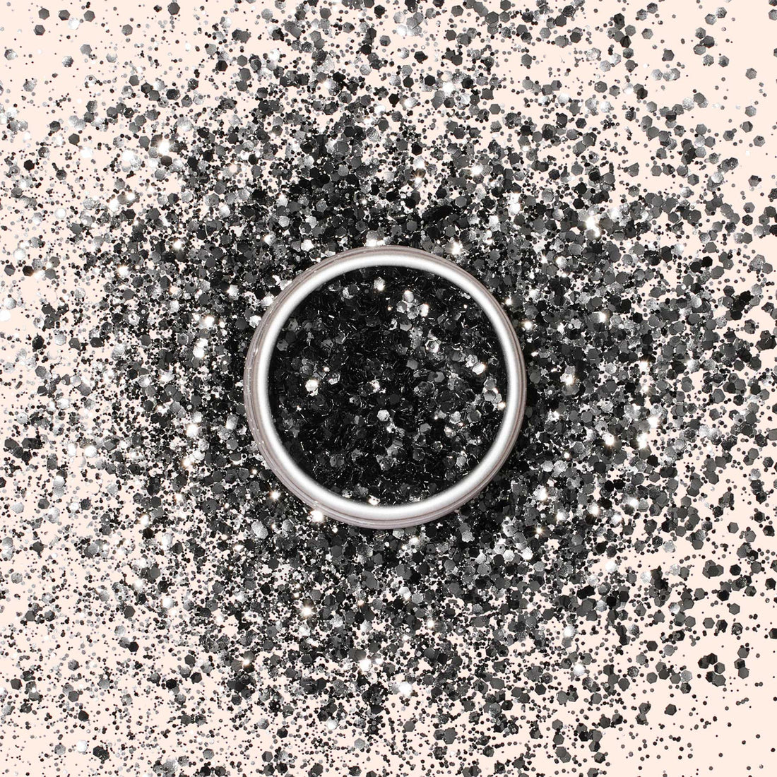 A silver ring rests on a light surface, encircled by scattered Manucurist Black Diamond Biodegradable Glitter, with a concentrated circle of this eco-friendly sparkle framing the ring at the center.