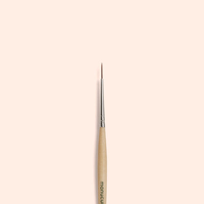 Le Liner Brush Manucurist, doté de poils synthétiques véganes et d’une pointe fine, est centré verticalement sur un fond beige clair uni.