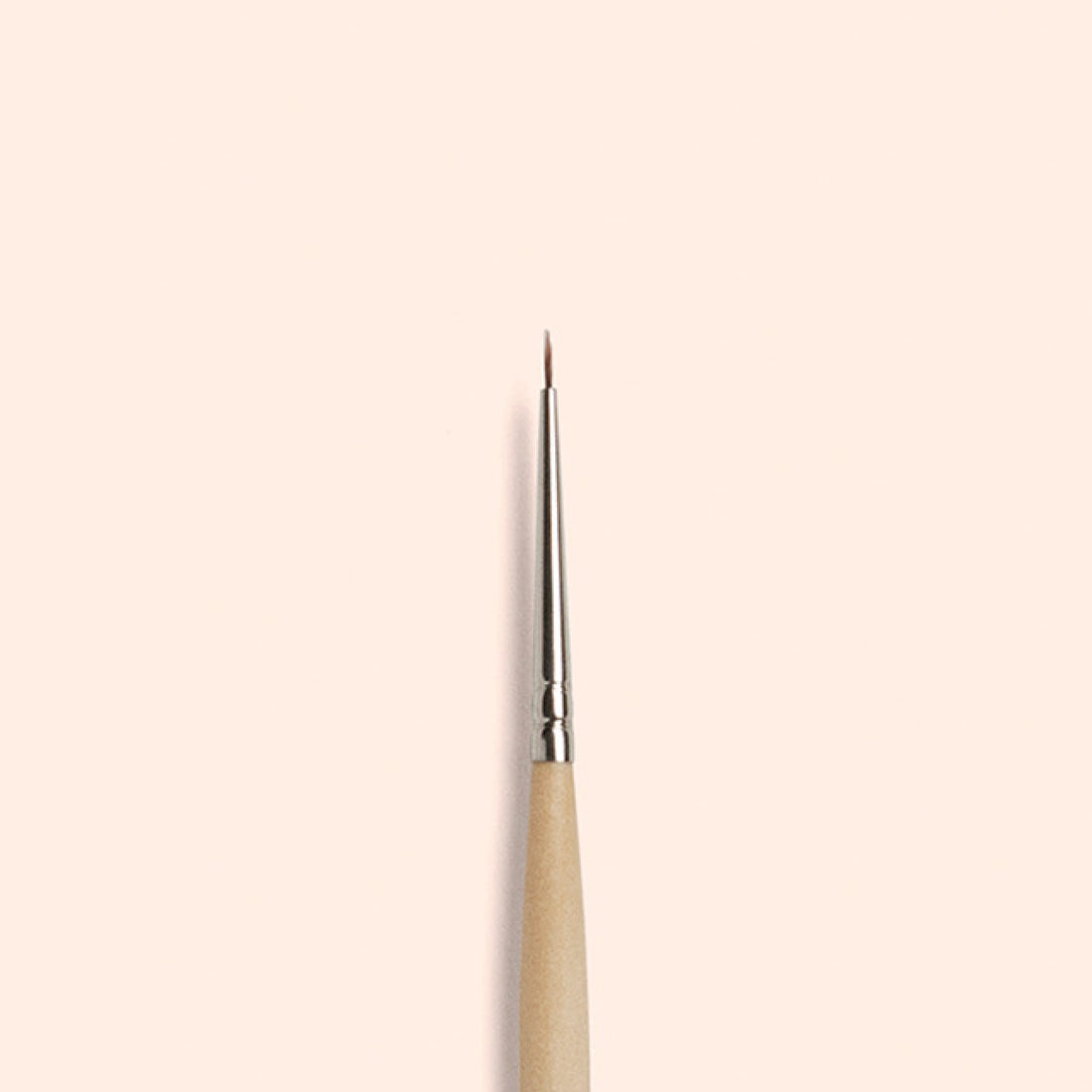 The Manucurist Fine Tip Brush, made with vegan synthetic bristles, a wooden handle, and a silver ferrule, stands vertically against a light beige background—perfect for creating precise nail art.