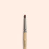 Manucurist’s Glitter Brush—a small brush with a wooden handle, metal ferrule, and soft vegan bristles—sits centered on a light beige background. The handle features "manucurist" branding, perfect for adding sparkle to your manicure.