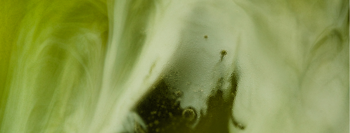 A close-up of green and white swirling patterns in liquid, creating a marbled, abstract effect with some darker and lighter areas blending together.