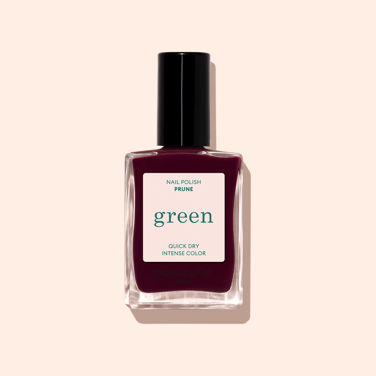 Un flacon de Prune de Manucurist, un vernis à ongles vintage à étiquette verte couleur prune profonde, au séchage rapide et à la couleur intense, présenté sur un fond beige pâle.