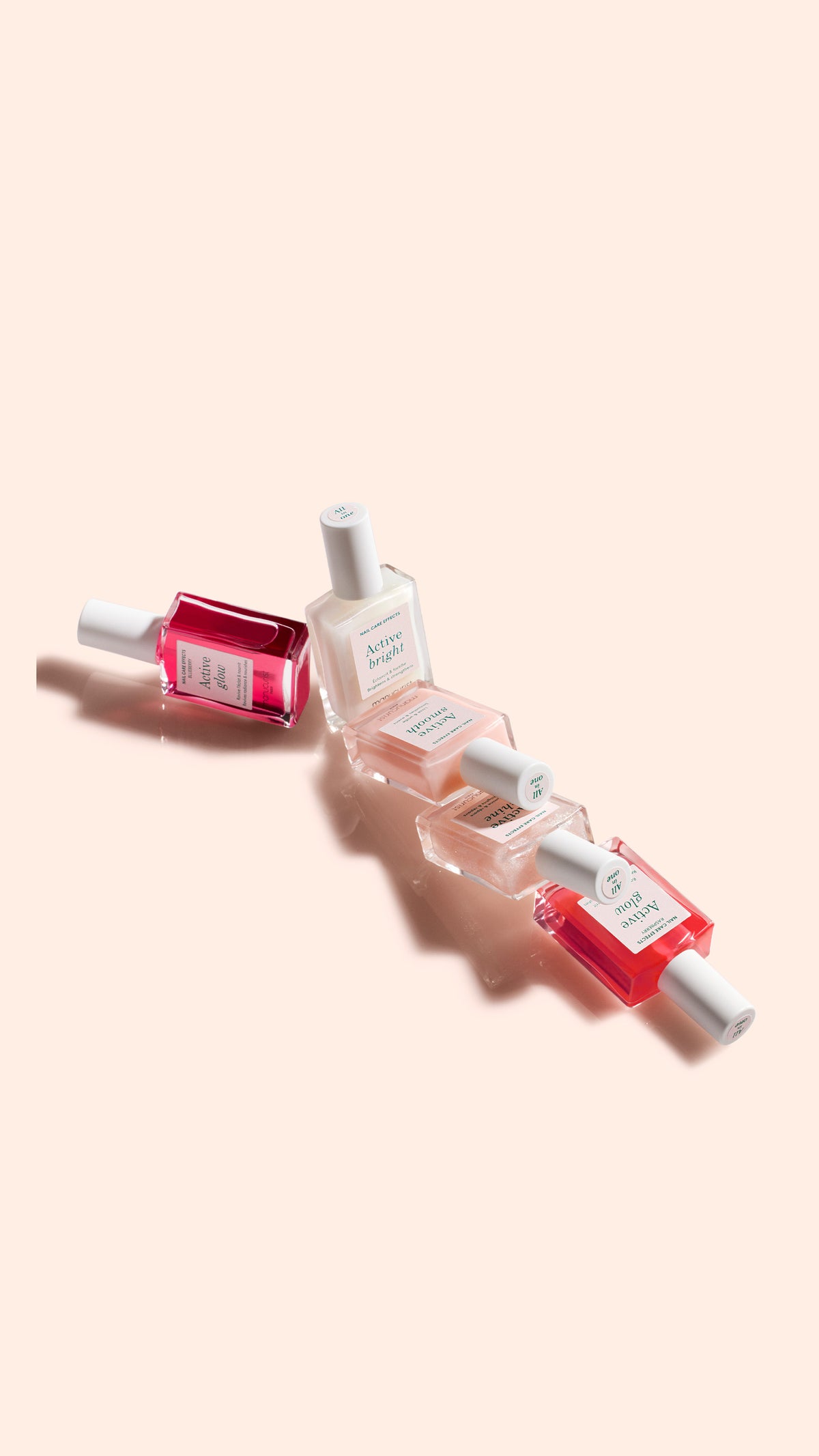 Five bottles of nail polish in various shades of pink and red are arranged diagonally on a light peach background, each bottle labeled with white caps and rectangular glass containers.
