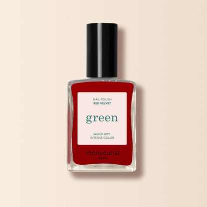 A bottle of Manucurist Red Velvet nail polish from the Green range, with a black cap and white "green" label, sits against a light beige background.