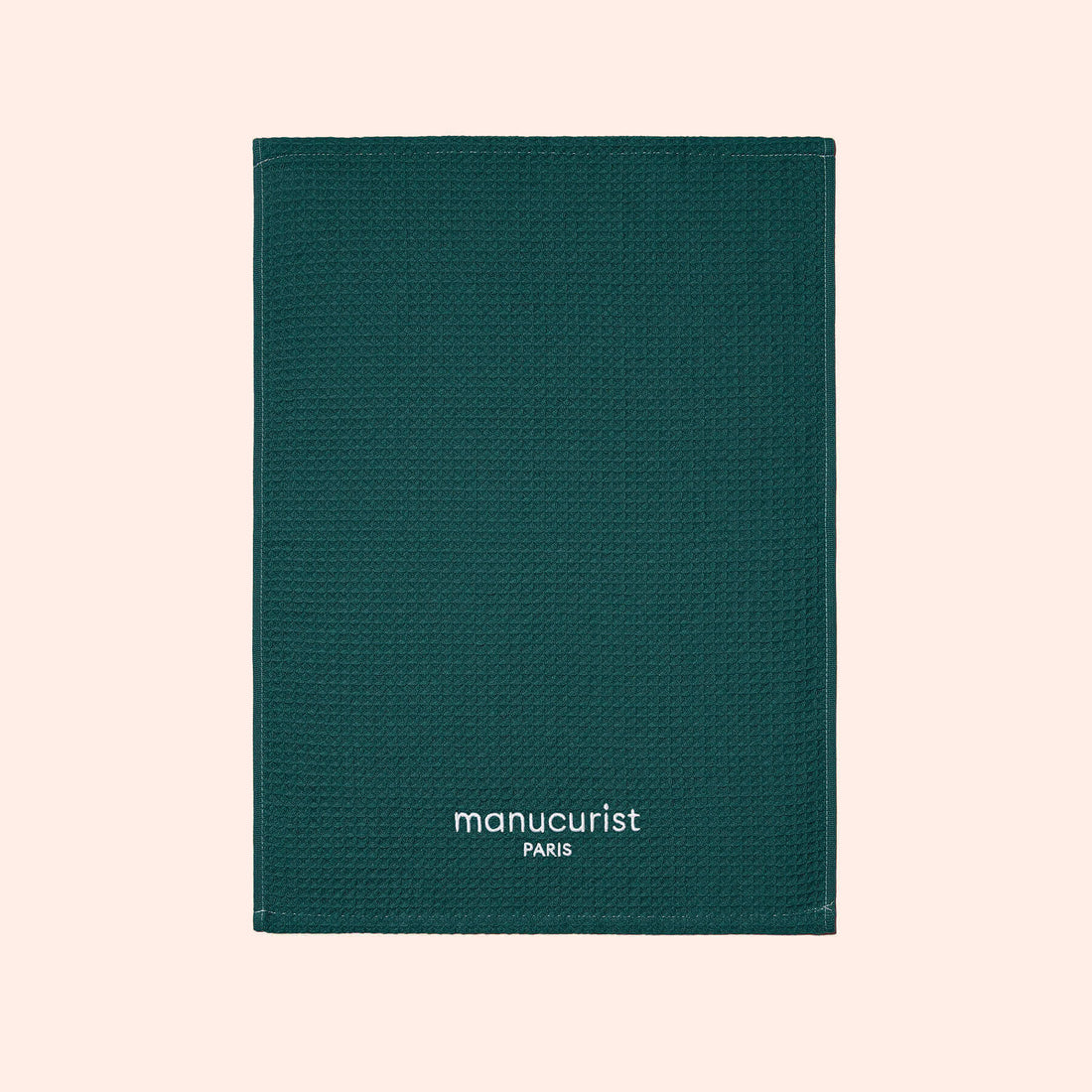 A green textured towel from Manucurist-us, featuring white "manucurist PARIS" text at the bottom center, displayed on a light beige background and ideal for surface protection.