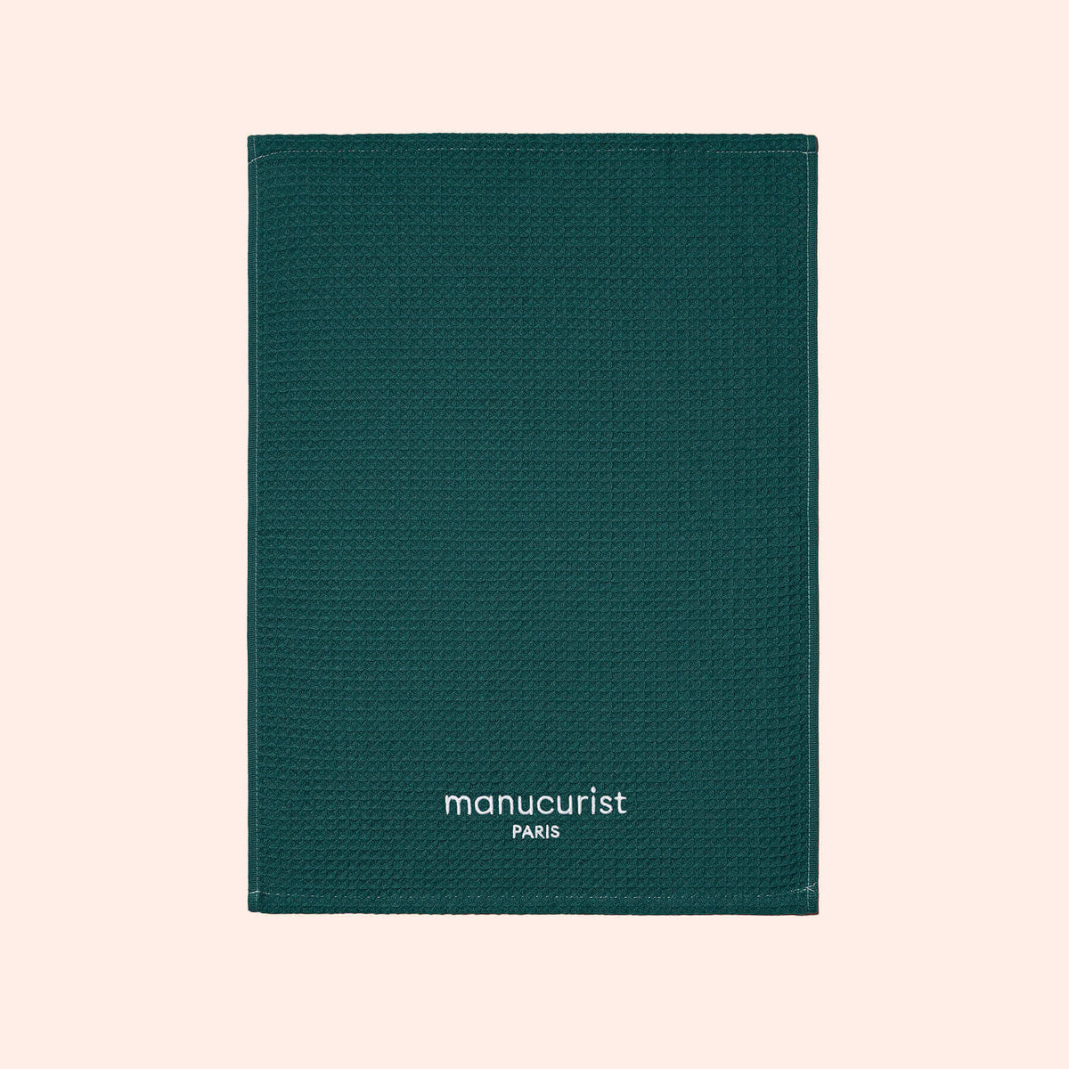 A green textured towel from Manucurist-us, featuring white "manucurist PARIS" text at the bottom center, displayed on a light beige background and ideal for surface protection.