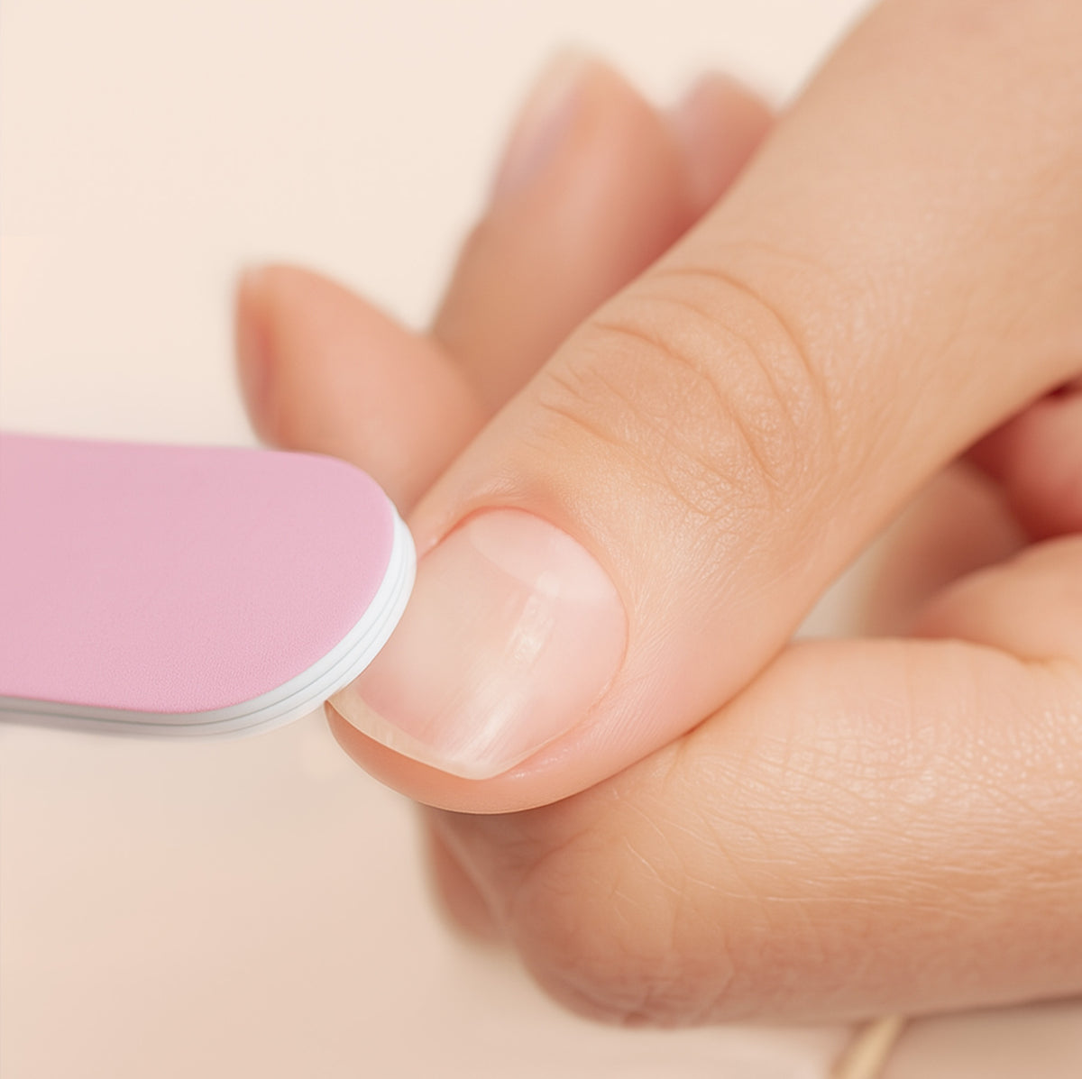 A close-up of a person filing their fingernail with a pink nail file, focusing on the hand and nail care process.