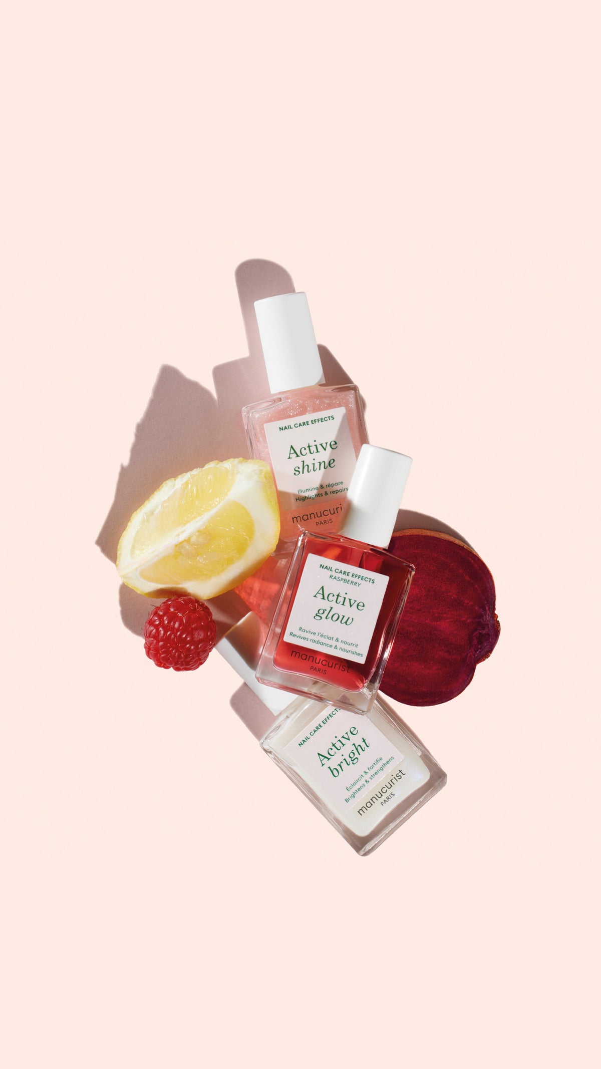 Three skincare serum bottles labeled Active Shine, Active Glow, and Active Bright are arranged with a lemon wedge, raspberry, and beetroot slice on a soft pink background.