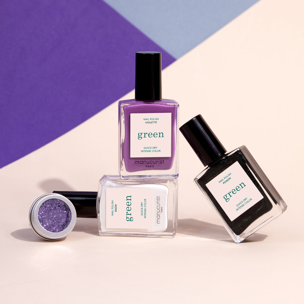 Three bottles of Manucurist’s Witchy  Wicked nail polish in purple, black, and clear, plus a pot of shimmery purple powder—perfect for Halloween nail art—are displayed on a geometric pastel background.