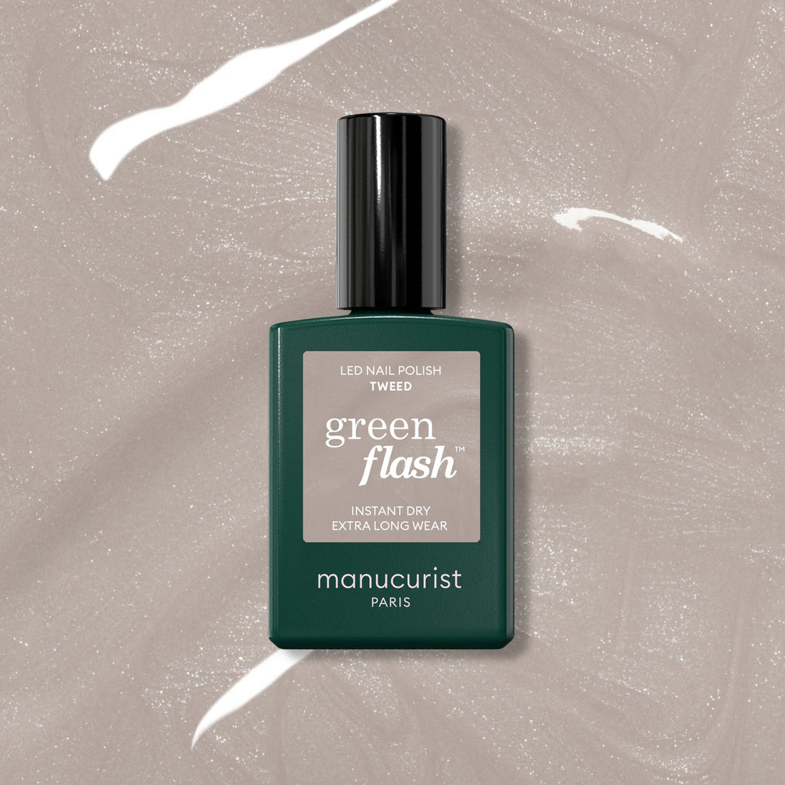Un flacon de vernis LED Green Flash Tweed Manucurist repose sur une surface beige scintillante, mettant en valeur son fini gris chaud nacré. Le flacon rectangulaire vert foncé est surmonté d&