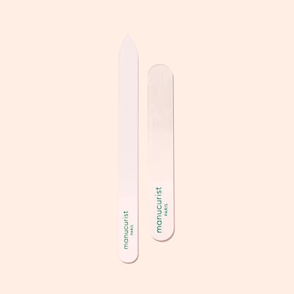 Two Manucurist-us Glass Nail Files, each with green "manucurist PARIS" text, are shown vertically on a light beige background. One file features a pointed end while the other has a rounded end.