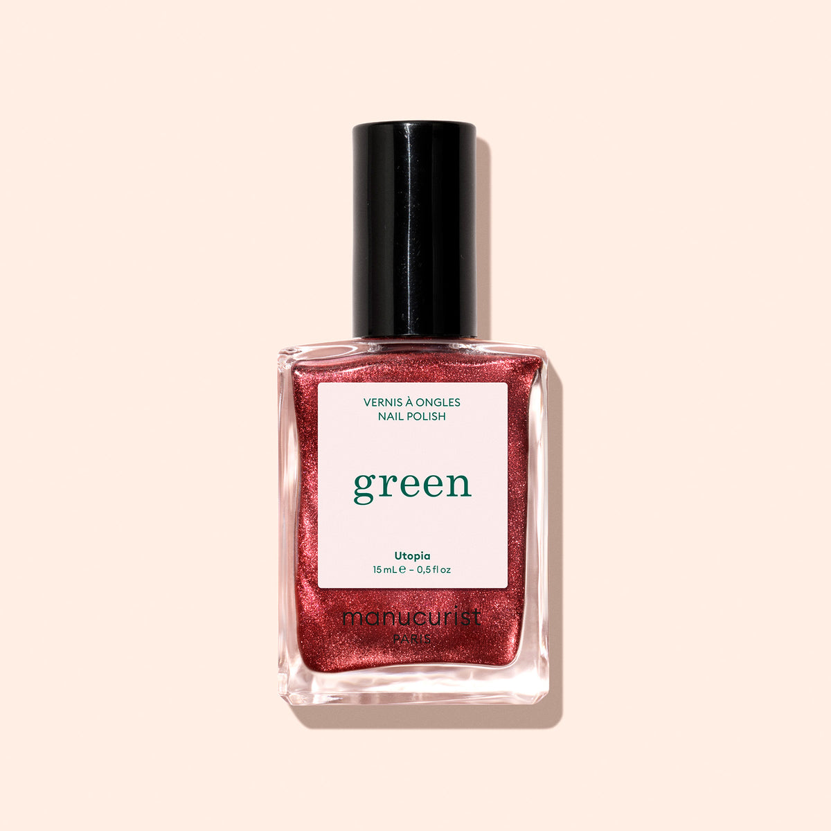 A 15 mL bottle of Manucurist Green™ nail polish in the shade Utopia, featuring a shimmery metallic crimson hue, is set against a light beige background. The label displays "Utopia" and product details.
