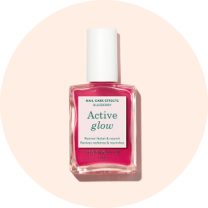 A bottle of pink nail polish labeled Active glow with a white cap, sitting on a pale peach background. The label mentions blueberry, flower, hibiscus, and neem and highlights care effects for nails.