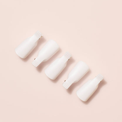 Five Manucurist-us Green Flash™ Remover Clips, perfect for gentle nail polish and gel polish removal, are arranged diagonally on a light beige background, evenly spaced with their open ends facing downward.
