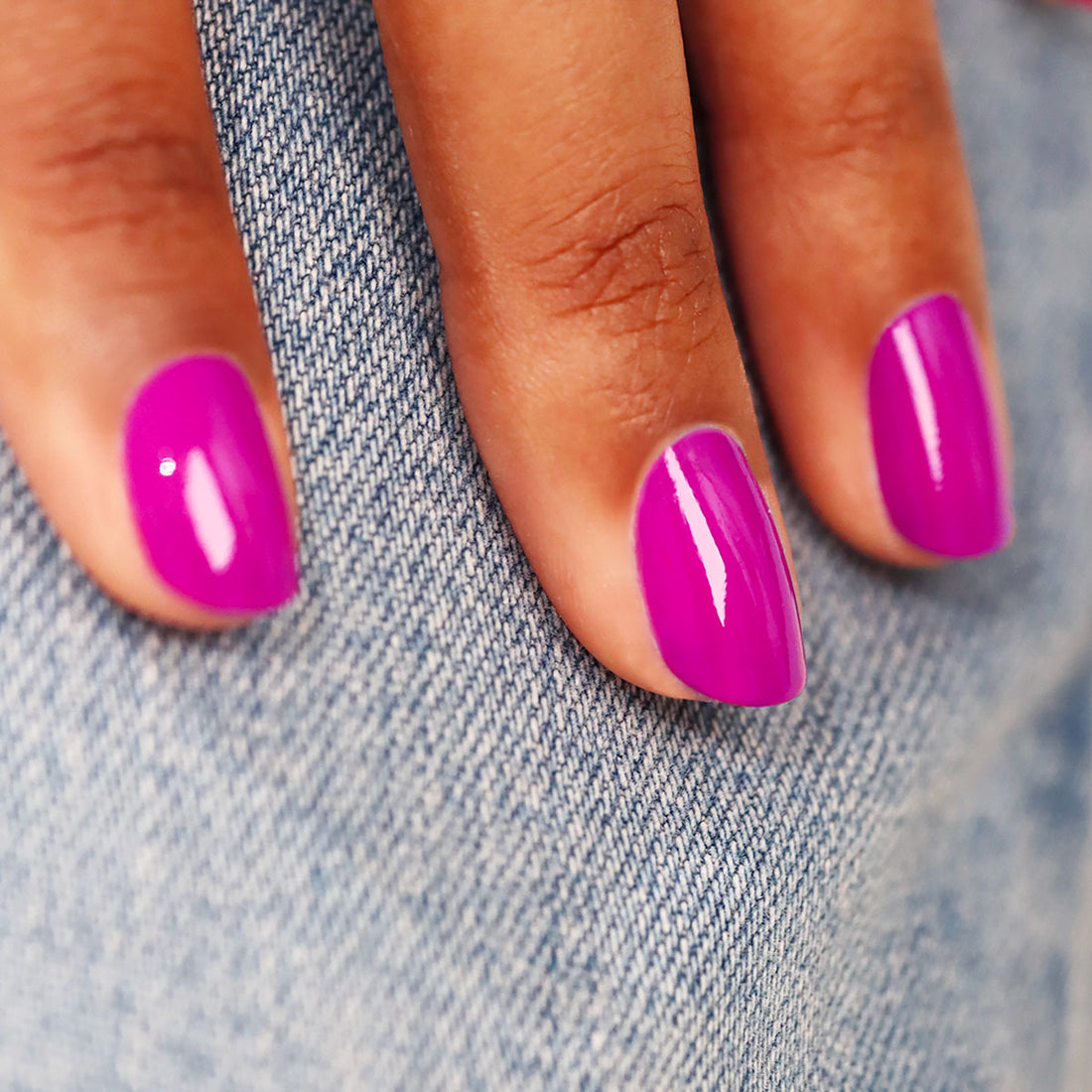 Gros plan sur une main aux ongles courts vernis avec Armeria de Manucurist, un vernis à ongles mauve rosé, posée sur un tissu en denim bleu clair.