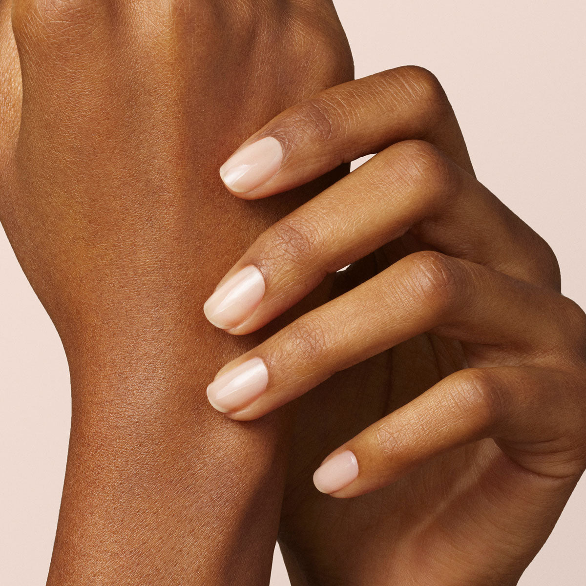 A close-up of a hand with neatly manicured nails painted in Manucurist’s Beige, a sheer natural pink nude gel polish, set against a light neutral background.