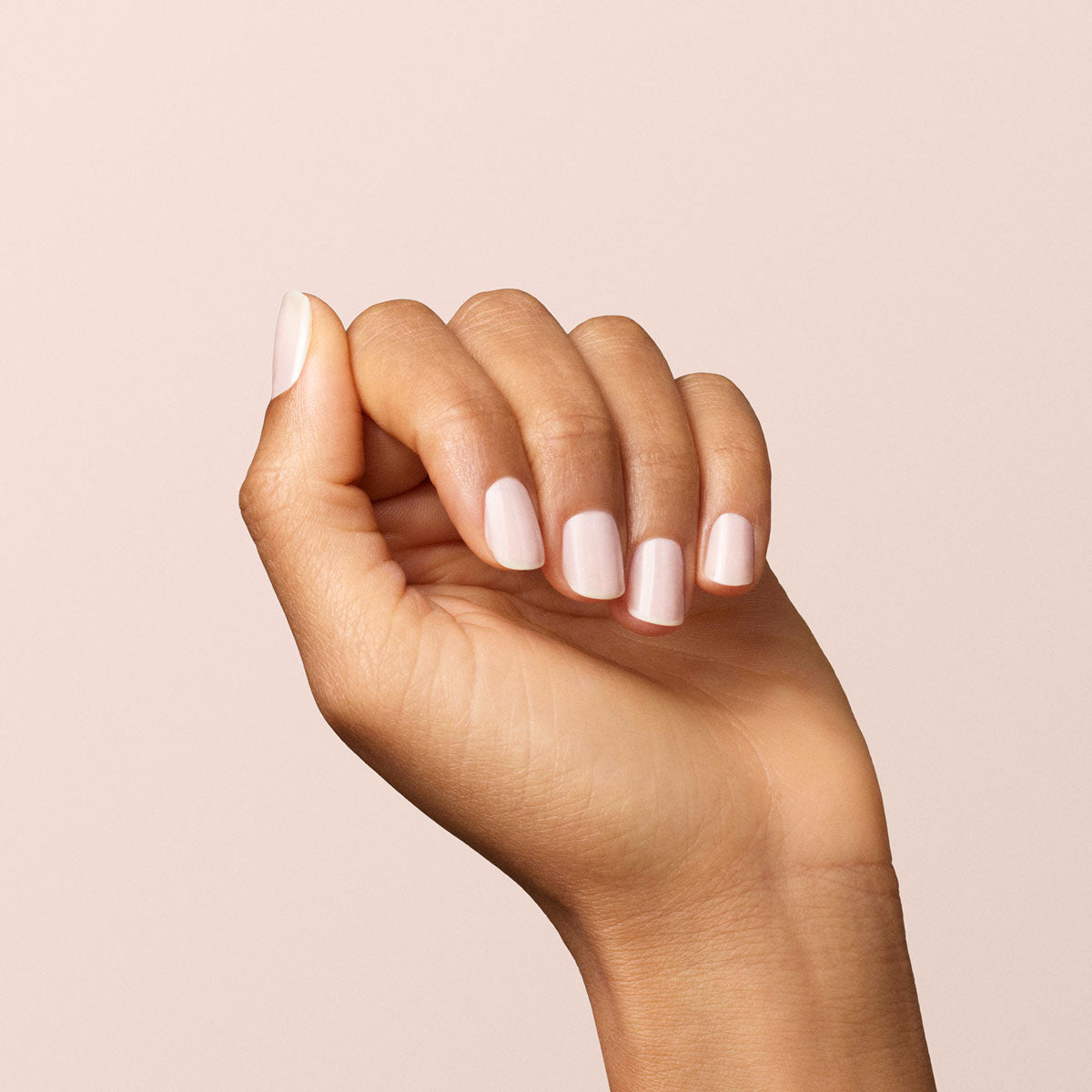 Une main aux ongles impeccablement manucurés avec la teinte Milky White de Manucurist, posée sur un fond beige clair uni.