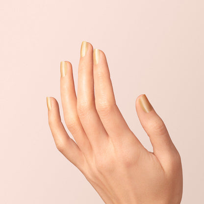 A hand with neatly manicured nails painted in Manucurist’s Gold Sand polish is held upright against a soft, light beige background.