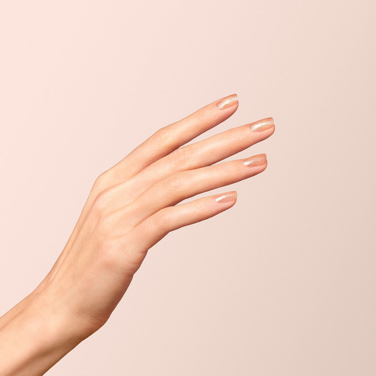 Une main aux ongles soigneusement manucurés, peints dans une teinte nude claire, présente des doigts détendus et une touche de scintillement du vernis à ongles Gold de Manucurist, sur un fond beige doux.