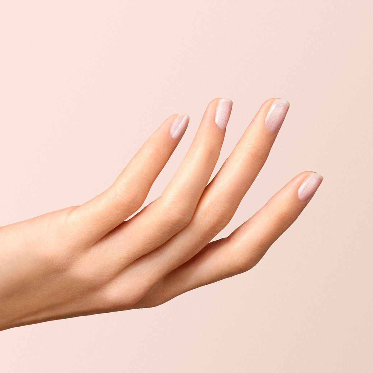 A hand with neatly manicured nails, some in light pink and others in Diamant shimmering silver gel polish by Manucurist, is displayed against a soft, pale pink background.