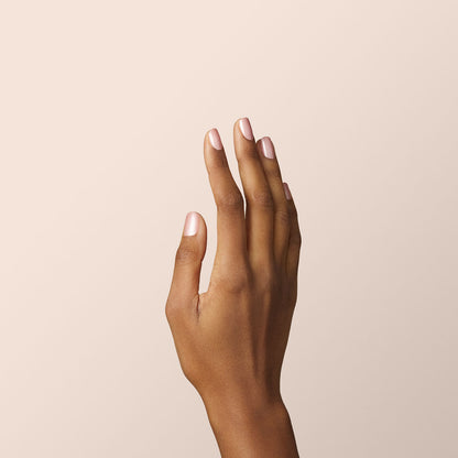 A hand with medium brown skin is held upright against a light beige background, fingers slightly spread and neatly trimmed natural nails—perfectly prepped for a Manucurist Carnation Green Flash gel polish manicure.