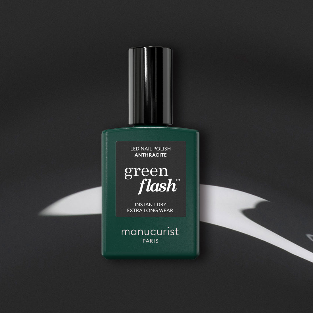 Manucurist’s Anthracite gel polish, a lustrous dark grey shade, is displayed on a black surface with white abstract highlights.