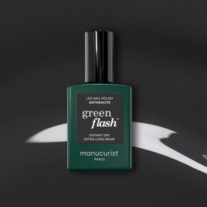 Manucurist’s Anthracite gel polish, a lustrous dark grey shade, is displayed on a black surface with white abstract highlights.