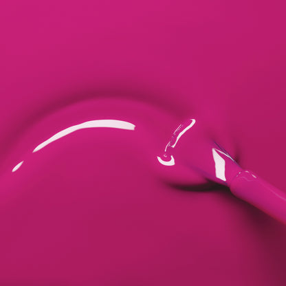 A Manucurist brush glides Armeria’s glossy, bright pink gel polish in a smooth curve across a matching pink background, revealing a shiny, reflective finish.