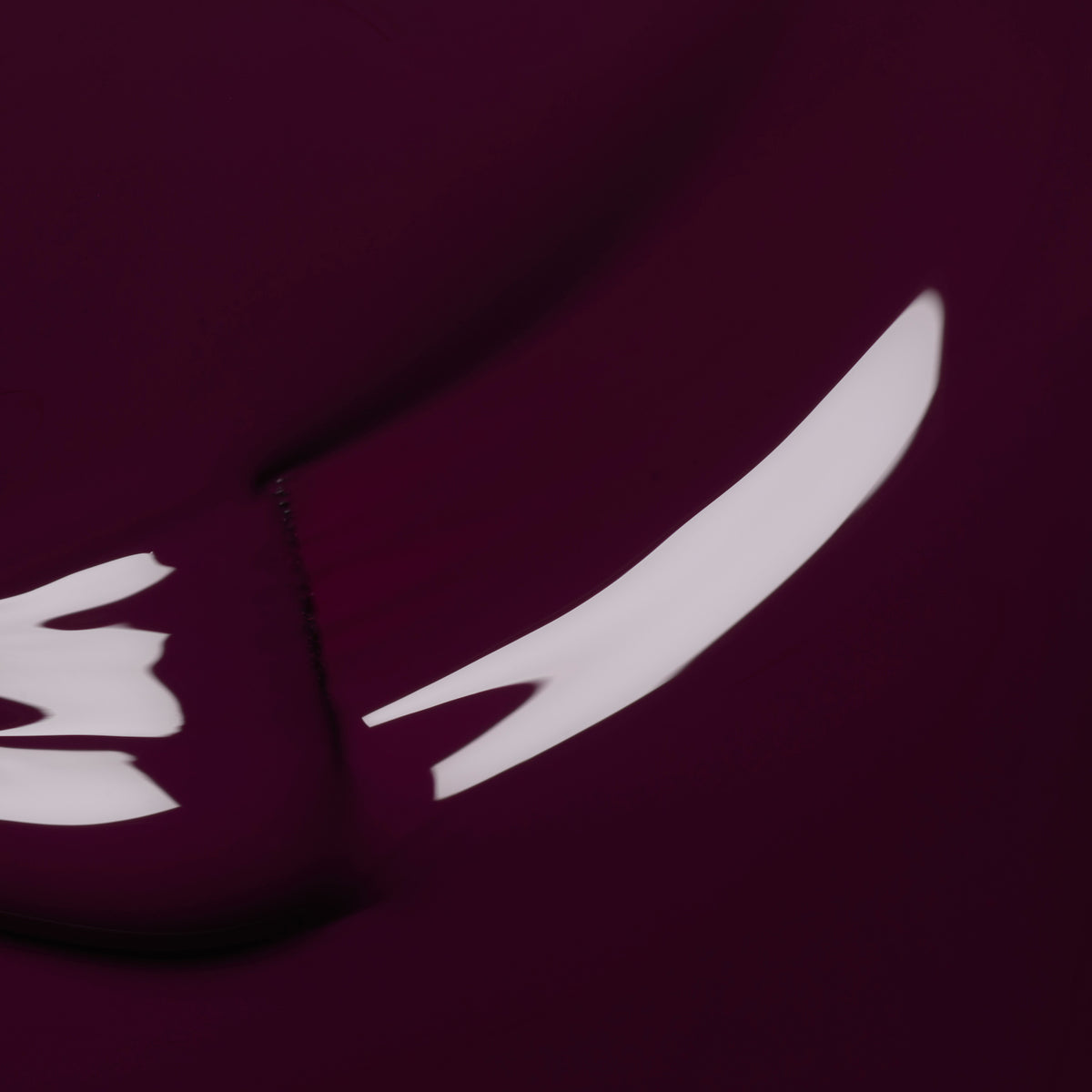 Minimalist close-up image with smooth, curved white reflections on a deep maroon background, echoing the look of Manucurist&