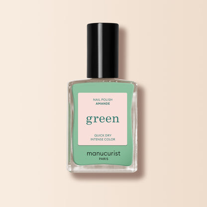 A bottle of Manucurist Amande nail polish from the Green™ range, featuring a mint green shade and black cap, labeled "Quick Dry Intense Color," is displayed on a light beige background.