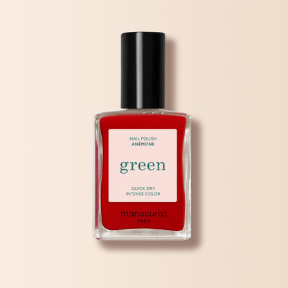 A bottle of Manucurist Anémone nail polish from the Green™ range, in a vibrant red shade, housed in a rectangular clear glass bottle with a black cap and a white label displaying product details.