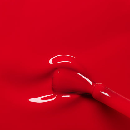 A close-up of Manucurist’s Poppy Red gel polish being applied, revealing a smooth, shiny layer of vibrant red color spreading evenly across the nail.