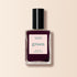 A bottle of Manucurist Aubergine nail polish, with a deep purple shade and a black cap, stands against a light beige background.