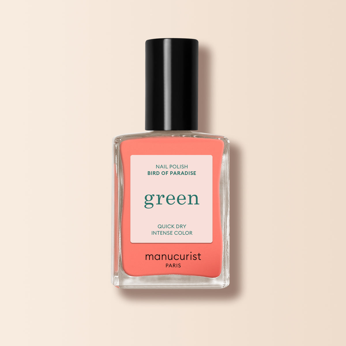 A bottle of Manucurist Bird of Paradise nail polish features a black cap and a white label with green and red text, shown on a soft beige background.
