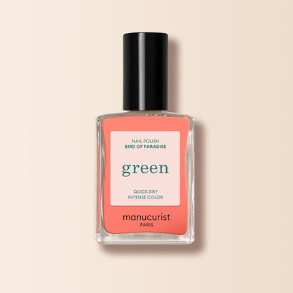 A bottle of Manucurist Bird of Paradise nail polish features a black cap and a white label with green and red text, shown on a soft beige background.