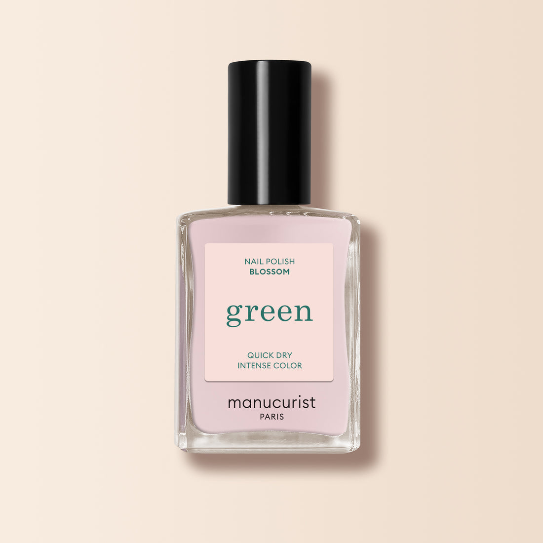 Un flacon de vernis à ongles Manucurist dans la teinte « Blossom », affichant une couleur rose clair crémeuse, un bouchon noir et un flacon carré en verre transparent de la gamme Green, est présenté sur un fond beige.
