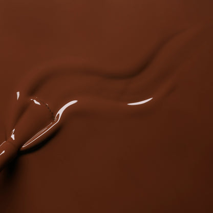 Close-up of smooth, melted chocolate in a warm brown hue being swirled, forming glossy waves that mirror the rich Chestnut shade of Manucurist&