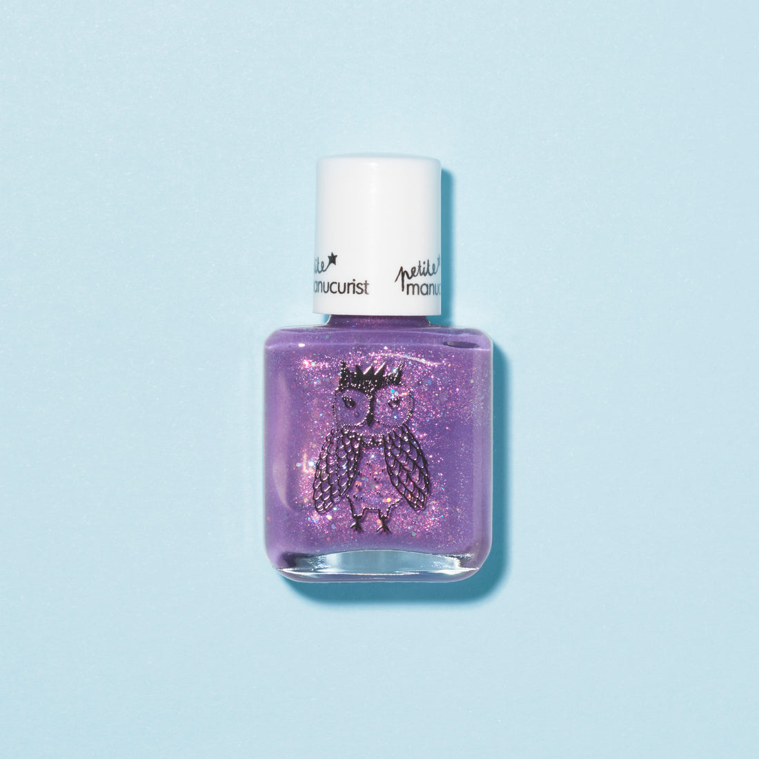 Un flacon de vernis à ongles pour enfants Manucurist Scarlett the Owl violet pailleté, avec un bouchon blanc et une illustration de chouette couronnée sur le devant, sur fond bleu clair.