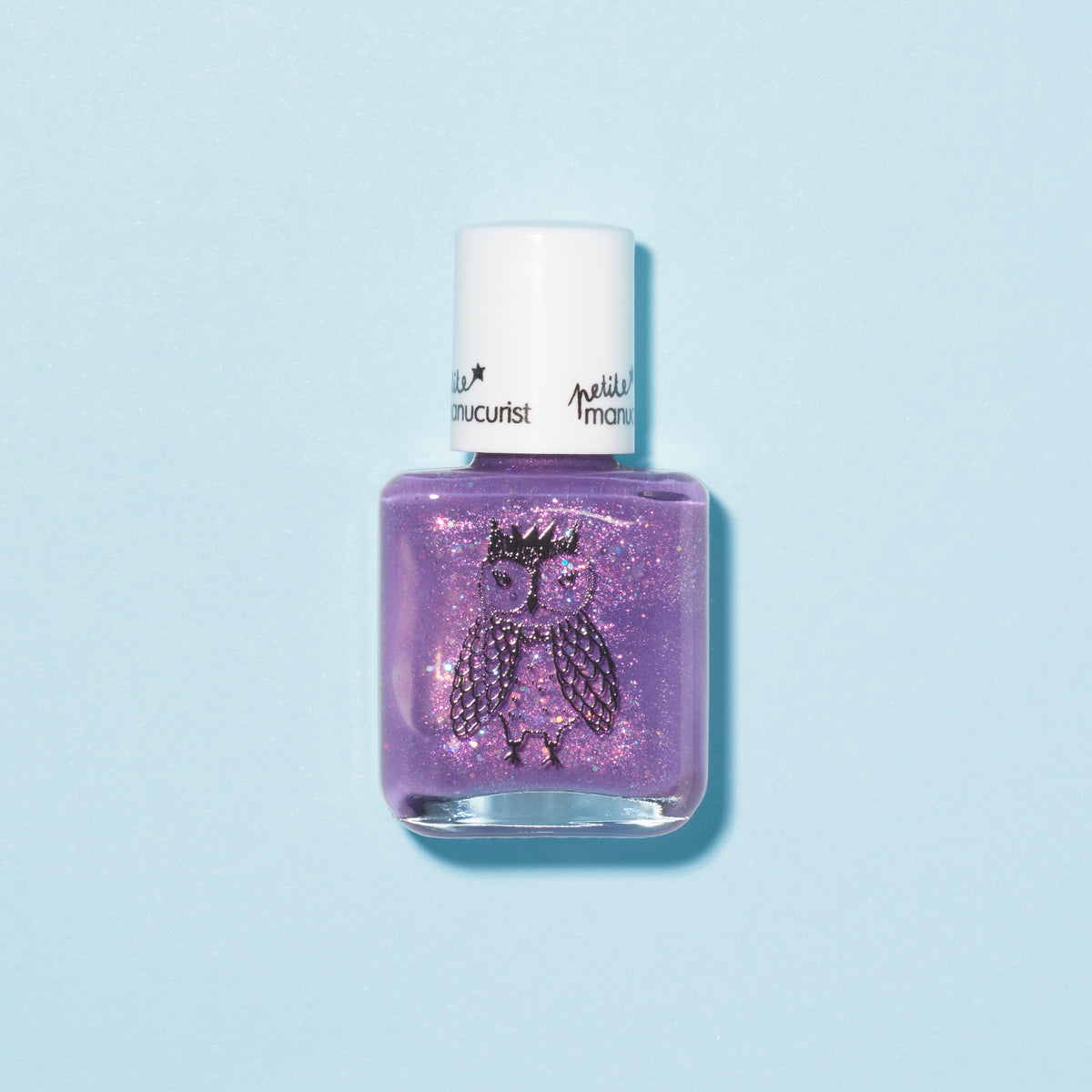 Un flacon de vernis à ongles pour enfants Manucurist Scarlett the Owl violet pailleté, avec un bouchon blanc et une illustration de chouette couronnée sur le devant, sur fond bleu clair.