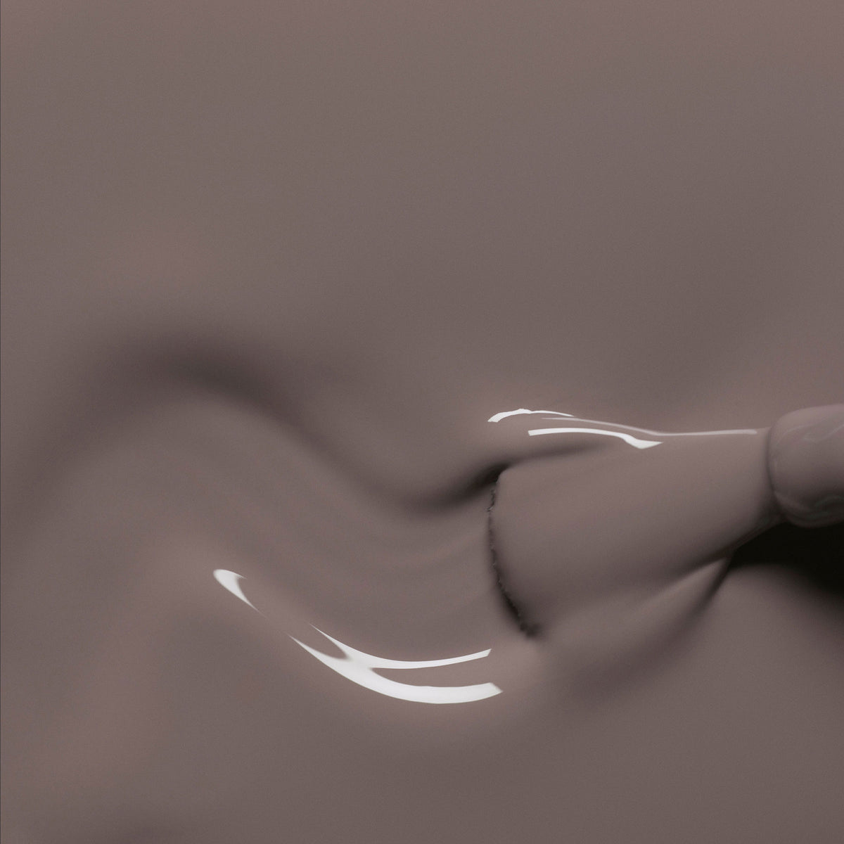 Gros plan d’un pinceau de vernis à ongles Manucurist Clay appliquant un gel taupe lisse et brillant sur une surface, formant de délicats tourbillons aux reflets lumineux.