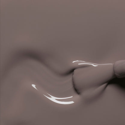 Gros plan d’un pinceau de vernis à ongles Manucurist Clay appliquant un gel taupe lisse et brillant sur une surface, formant de délicats tourbillons aux reflets lumineux.