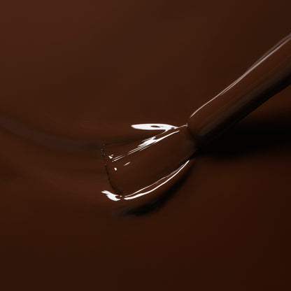 A close-up of a nail polish brush dipping into Manucurist’s Clove, a glossy chocolate brown gel polish, with smooth, shiny liquid coating the bristles.