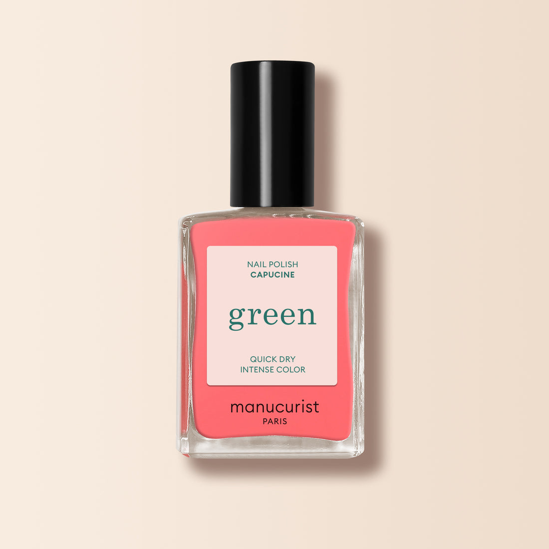 Un flacon de vernis à ongles Manucurist dans la teinte Capucine, rose corail de la gamme Green, avec un bouchon noir et l’inscription "green, quick dry intense color" sur l’étiquette, présenté sur un fond beige doux.