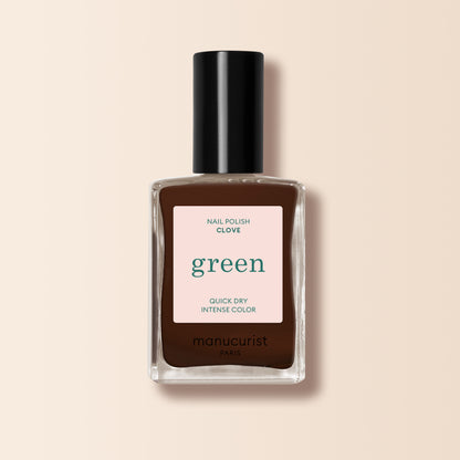 A bottle of Manucurist Clove nail polish, a chocolate brown shade from the Green™ range, features a black cap and a label reading "green, quick dry intense color" on a light beige background.