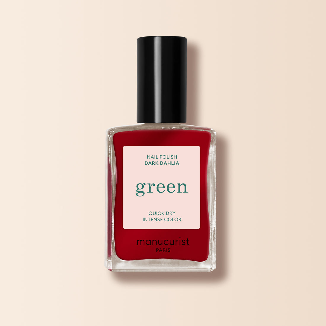 Un flacon de vernis à ongles rouge foncé Manucurist Dark Dahlia, présenté dans une bouteille rectangulaire en verre avec un bouchon noir et une étiquette blanche, sur fond beige.