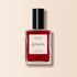 Un flacon de vernis à ongles rouge foncé Manucurist Dark Dahlia, présenté dans une bouteille rectangulaire en verre avec un bouchon noir et une étiquette blanche, sur fond beige.